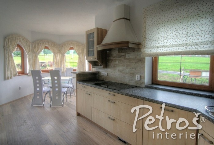 K ROVNÝM LINIÍM MODERNÍ KUCHYNĚ S JÍDELNOU hezky sluší i poněkud romantičtější jemně vyšívané závěsy s přírodním motivem, zřasené na jednoduchou řasící pásku a stažené do ledvinkových úvazů. Je to trochu extravagantní kombinace, ale přesto - nebo právě proto - dodala tomuto modernímu interiéru osobité kouzlo a příjemnou nepřeplácanou měkkost. Římská roleta nad kuchyňskou linkou, která je vyrobena ze stejné vyšívané látky, jako závěsy, je nejen krásná a stylová, ale také velmi praktická.